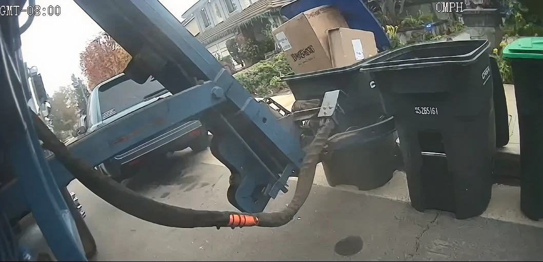 Camera view from a residential collection truck picking up bins at the curb